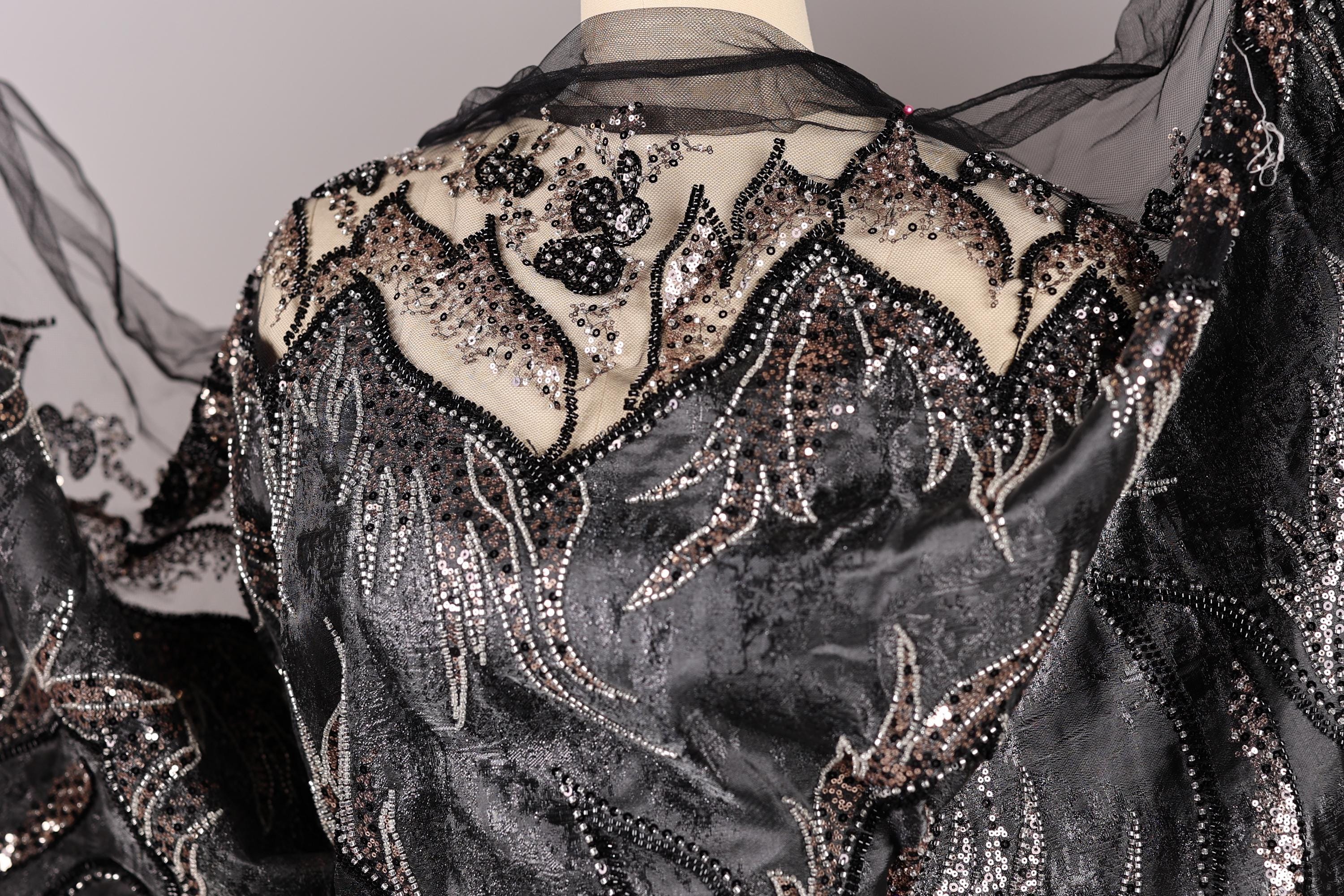 a close-up view of a black and silver sequined dress with intricate embroidery and beading details.