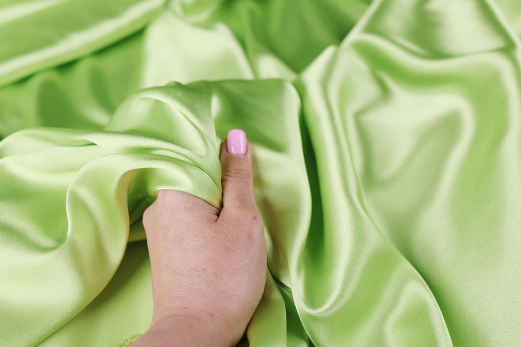 a woman&#39;s hand on a green satin fabric