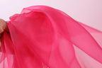 A close-up view of a hand holding a piece of pink fabric, with the fabric's folds and creases visible.