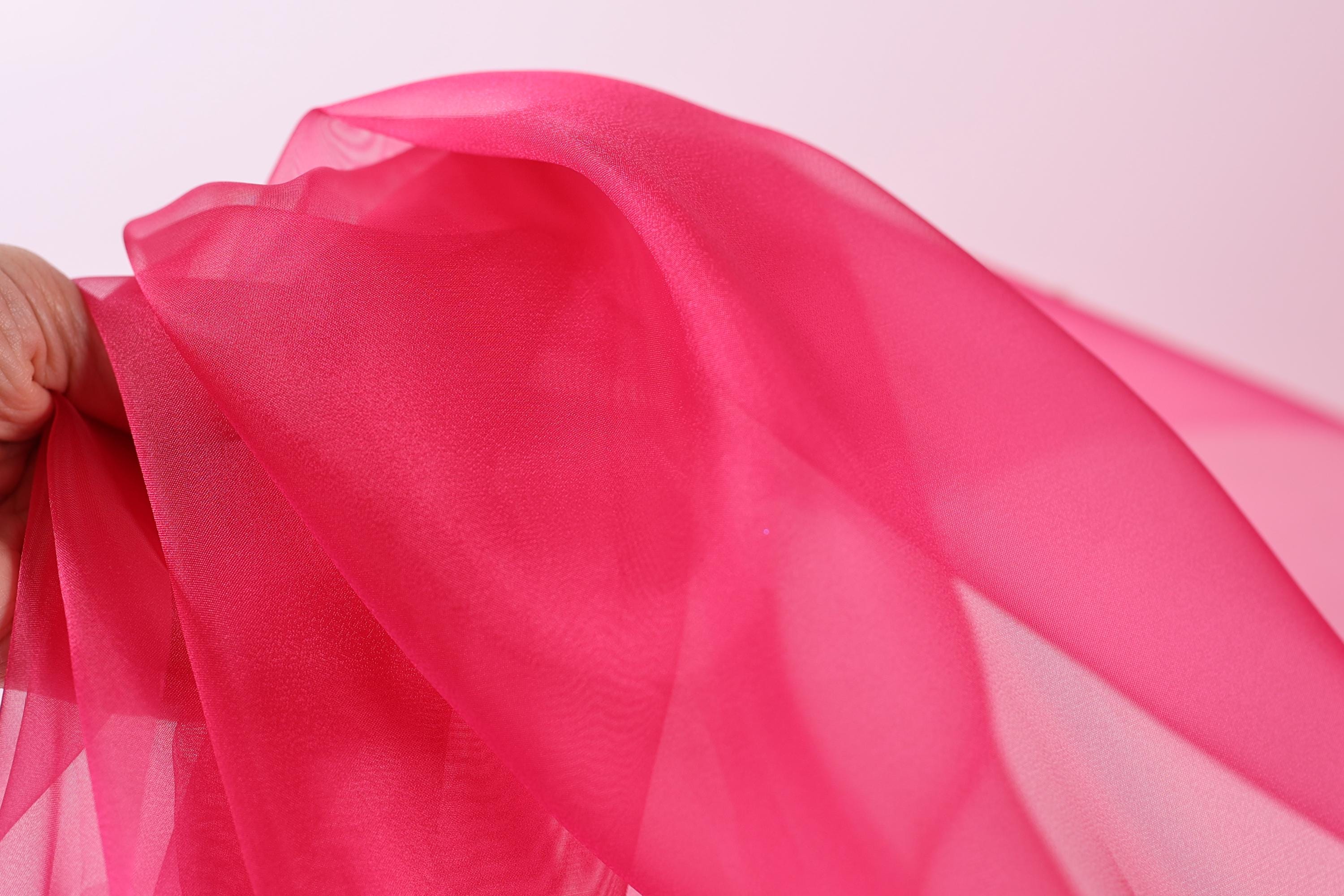 A close-up view of a hand holding a piece of pink fabric, with the fabric's folds and creases visible.