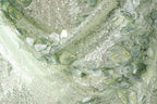 The image is a close-up of a fabric with a floral pattern, featuring green and white colors and small sequins or glitter accents.