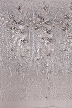a close-up view of a fabric with a floral pattern, including small white flowers and leaves. The fabric appears to be made of a shiny, metallic material, giving it a metallic or metallic-like appearance. The pattern is intricate and detailed, with the flowers and leaves arranged in a repeating design across the fabric.