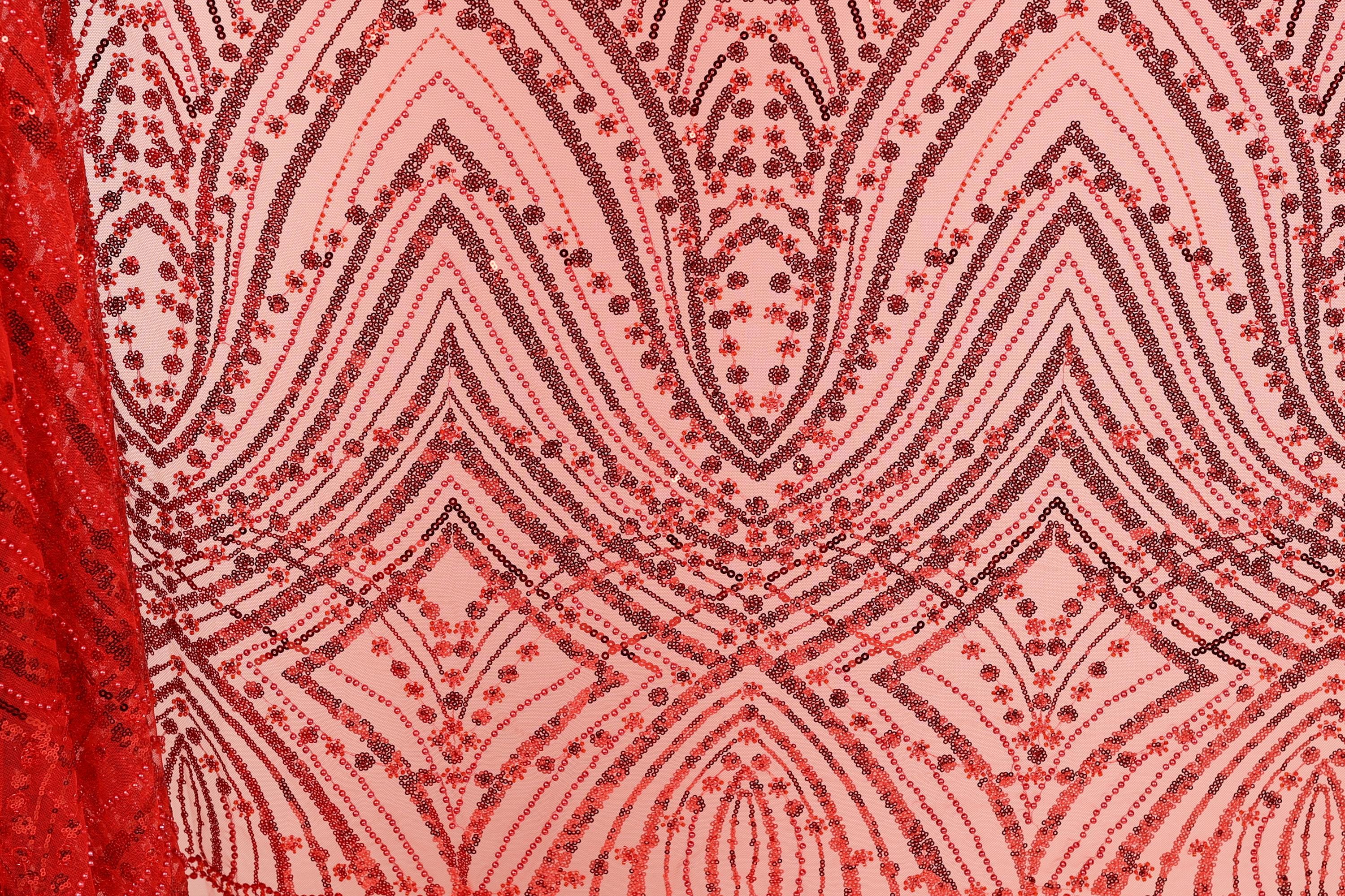a close-up view of a fabric with a repeating pattern of red and black sequin designs. The pattern consists of various shapes and lines, creating a visually striking and intricate design. The fabric appears to be a piece of clothing or textile, with the red and black colors standing out prominently against the pink background.