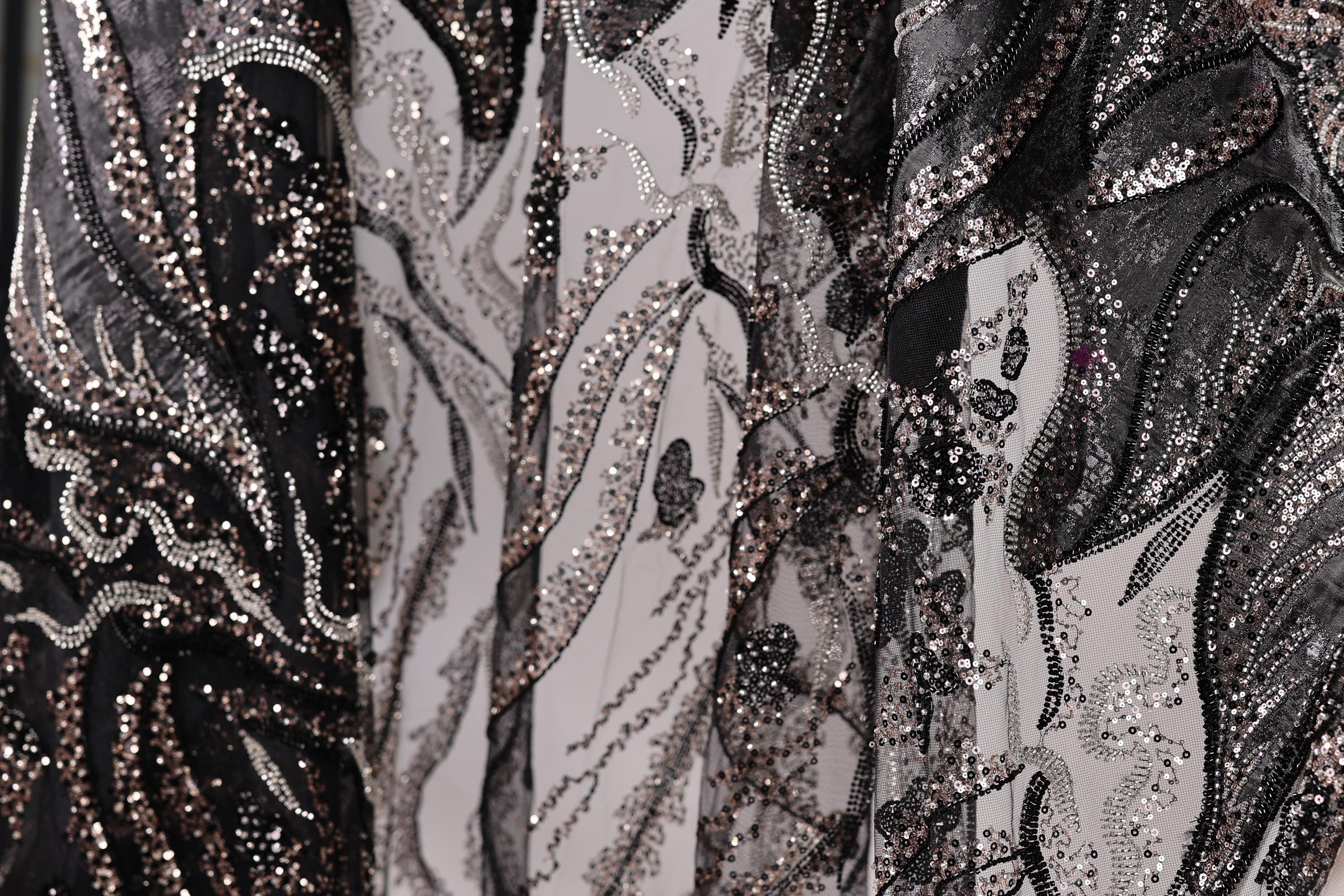The image is a close-up of a fabric with a black and white pattern, featuring a mix of glittering and metallic elements.