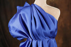 A close-up view of a blue one-shoulder dress with a draped, flowing fabric and a ruched neckline.