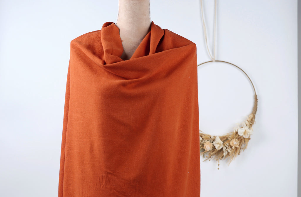 a mannequin wearing a bright orange scarf, with a wreath hanging on the wall behind it.