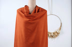 a mannequin wearing a bright orange scarf, with a wreath hanging on the wall behind it.