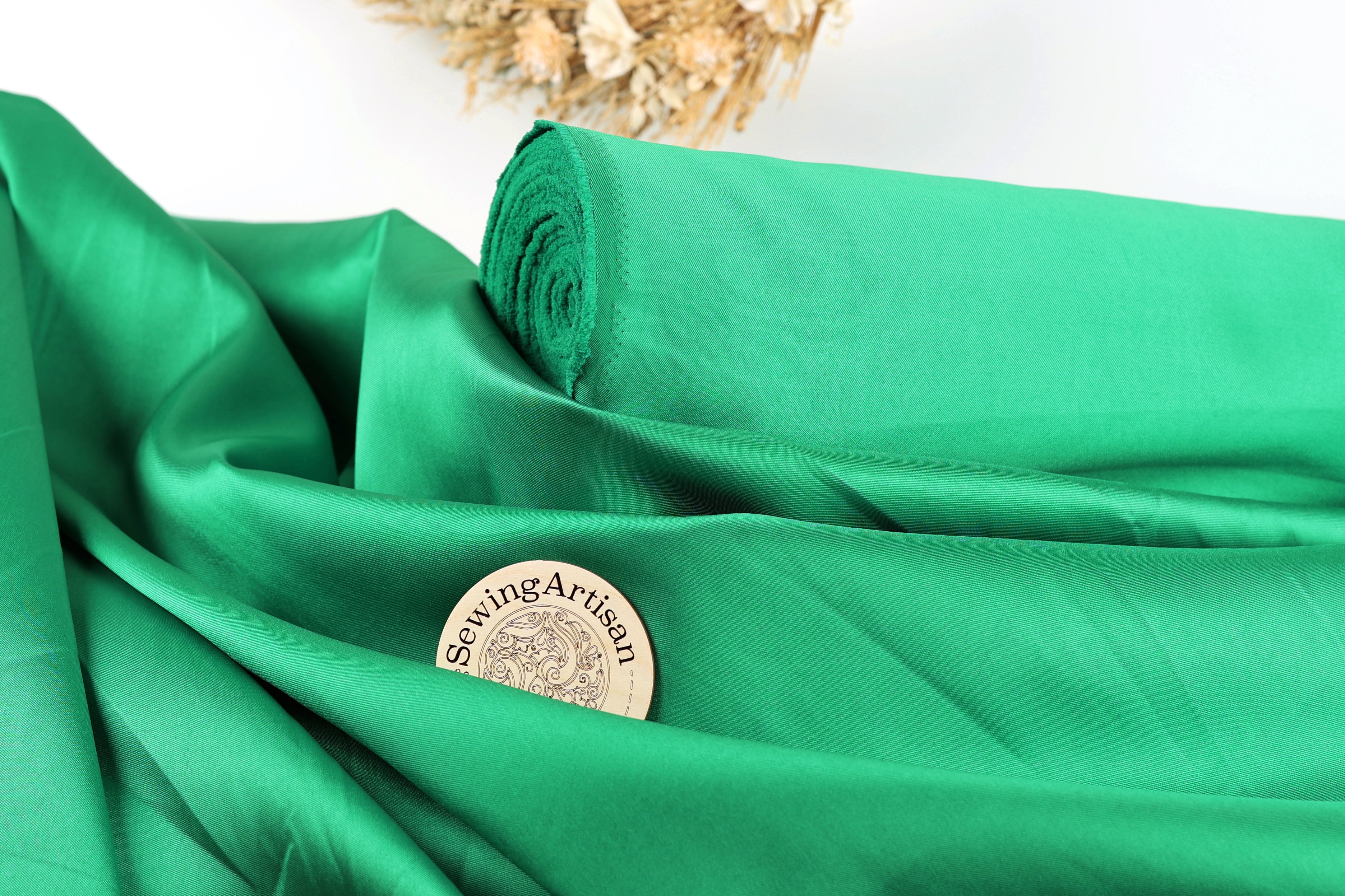 a close-up view of a green fabric, possibly silk, with a small round label or badge placed on it. The background is blurred, but it appears to be a white surface.