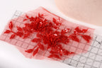 a red floral embroidery with sequins, placed on a transparent surface.