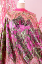 a vibrant, intricately designed fabric with a mix of pink, green, and gold colors. The fabric appears to be a sheer material, with a floral pattern and sequin accents. The design is detailed and eye-catching, showcasing the craftsmanship and artistry involved in creating this piece of clothing or textile.