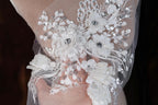 A close-up view of a delicate, intricately embroidered white lace piece, featuring a floral design with small, sparkling embellishments.
