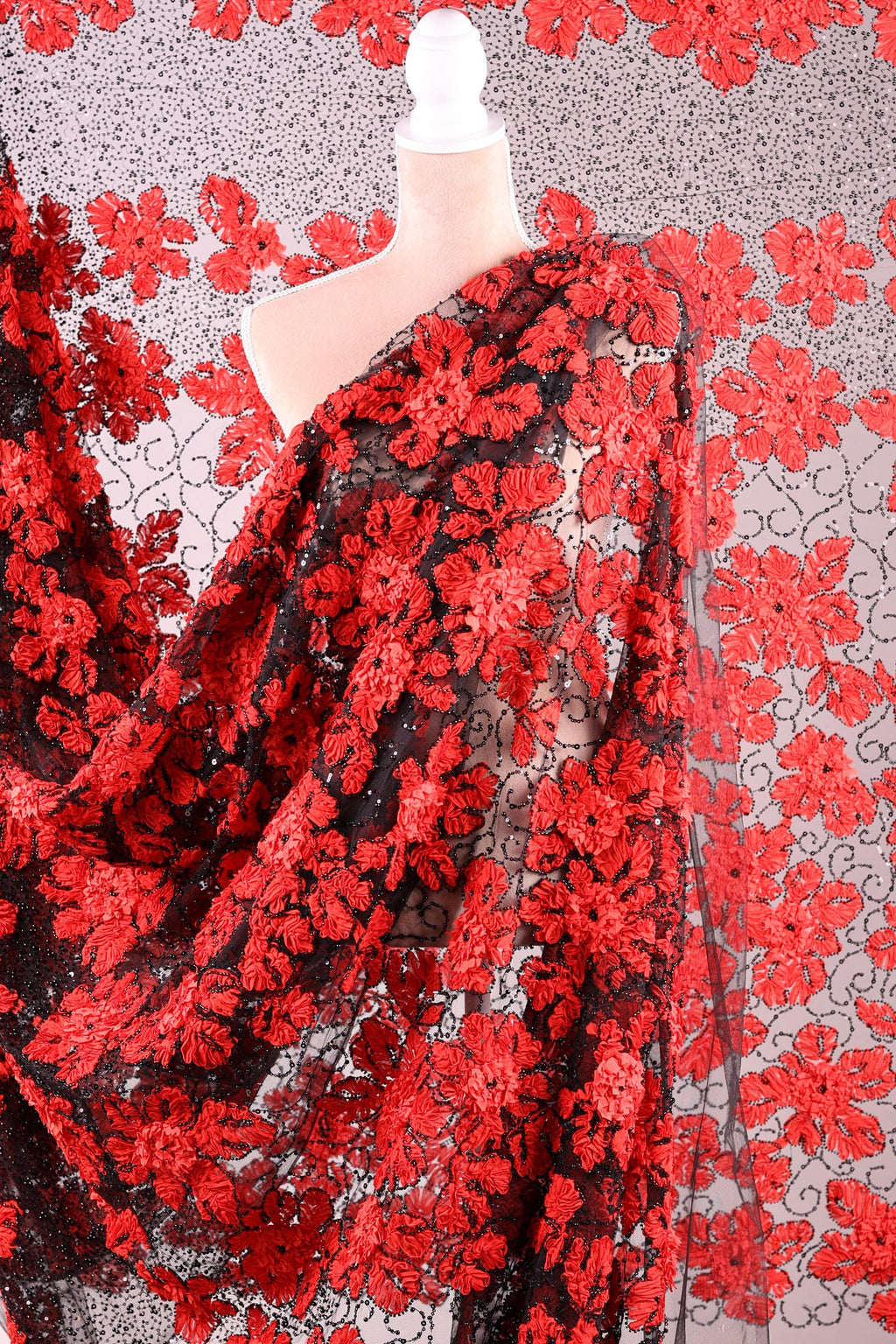 a close-up view of a fabric with a striking red floral pattern. The fabric appears to be a sheer material, with a black background that contrasts with the vibrant red of the flowers. The fabric is spread out, creating a sense of depth and texture in the image.