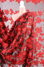 a close-up view of a fabric with a striking red floral pattern. The fabric appears to be a sheer material, with a black background that contrasts with the vibrant red of the flowers. The fabric is spread out, creating a sense of depth and texture in the image.