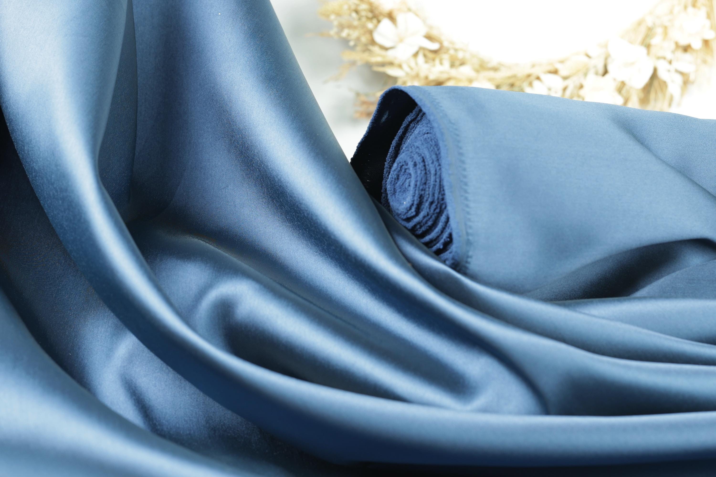 a close-up view of a blue satin fabric, with a blurred floral background.