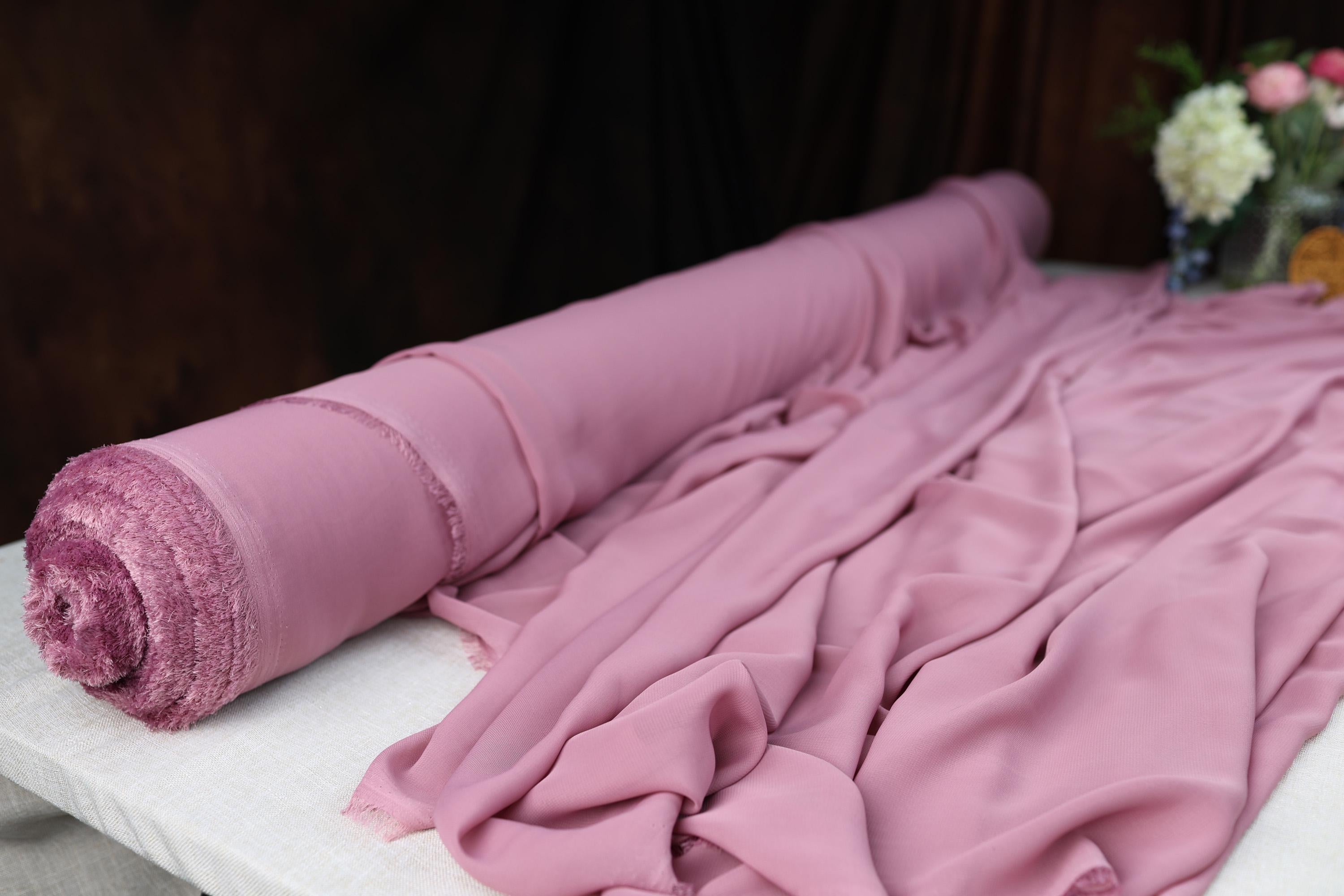 a rolled up pink blanket sitting on top of a bed