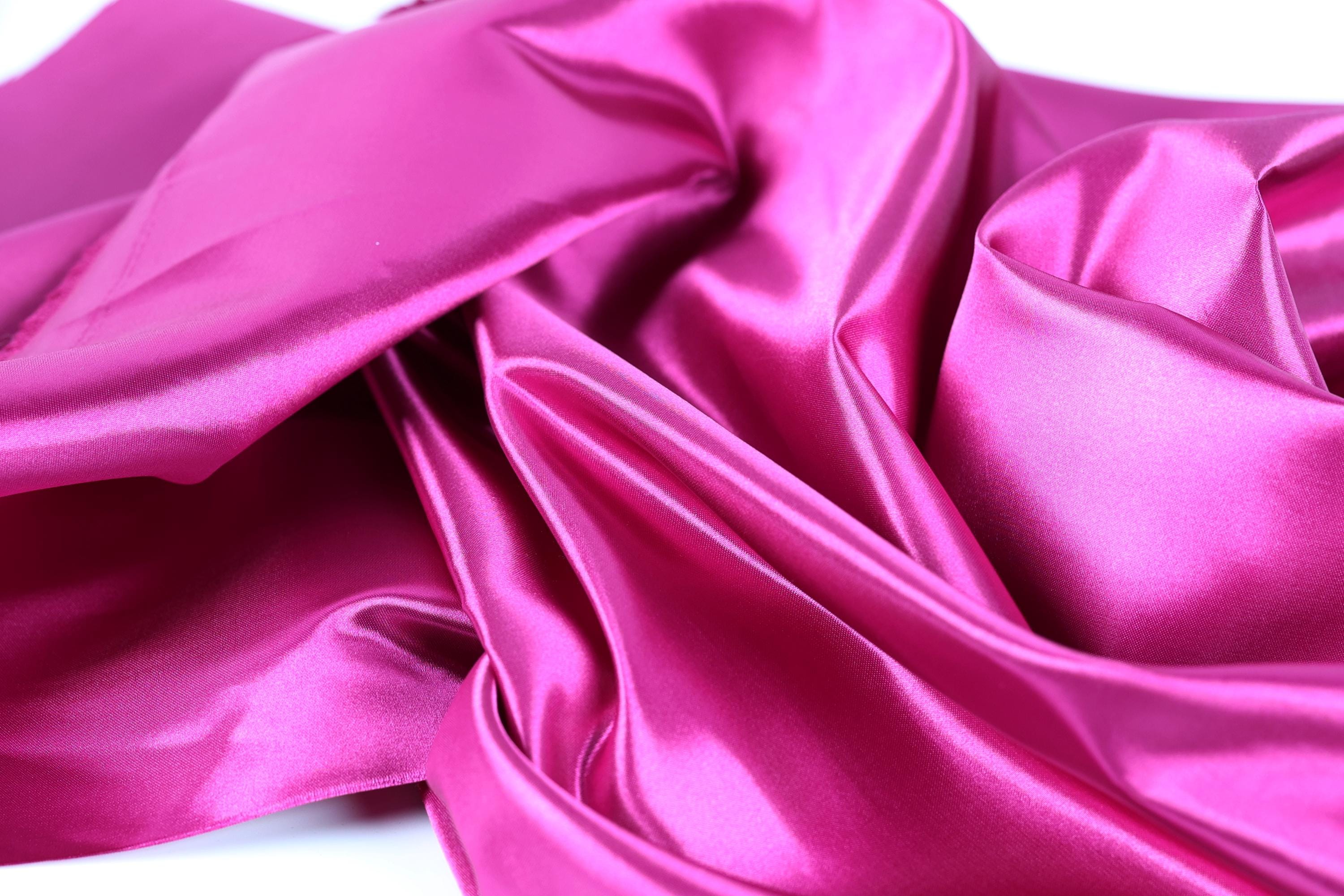 The image is a close-up of a shiny, smooth, and vibrant pink satin fabric.