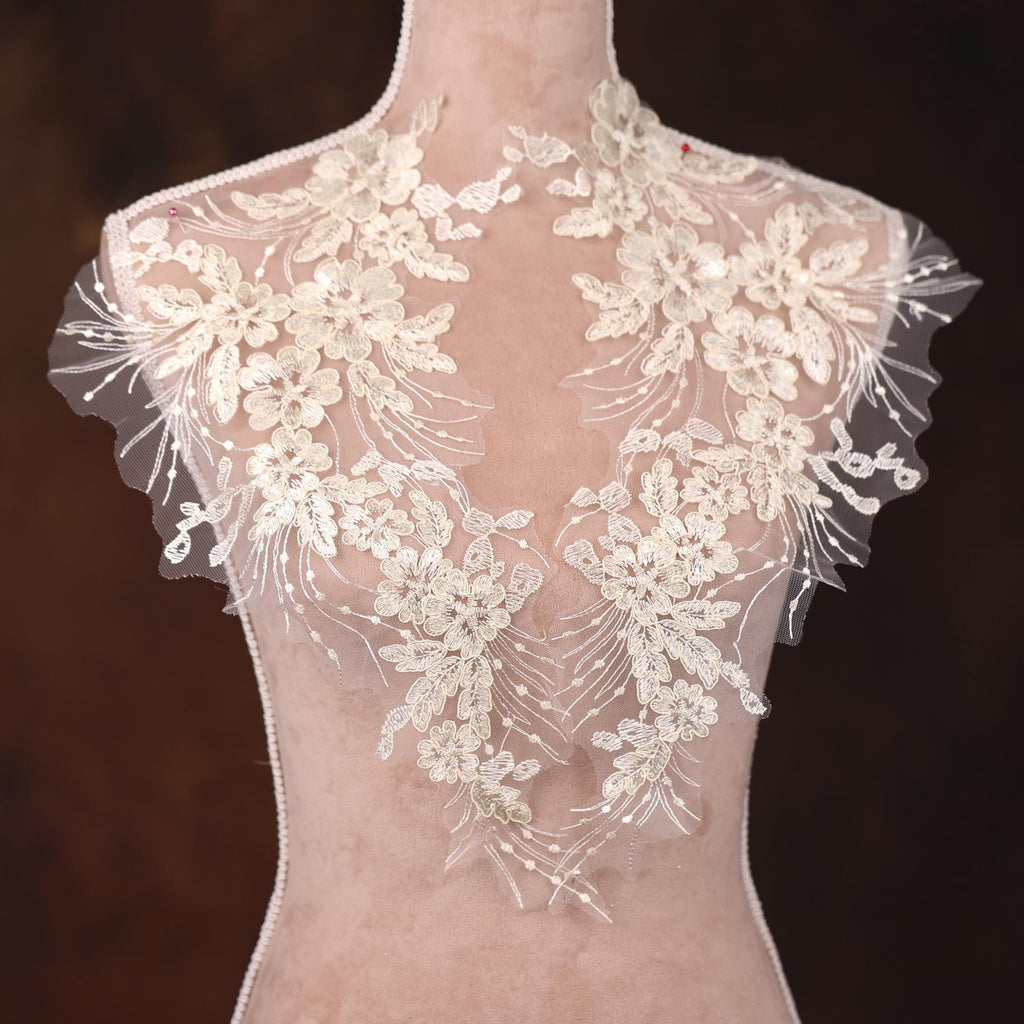 A mannequin wearing a white lace dress with intricate floral embroidery on the neckline and sleeves.
