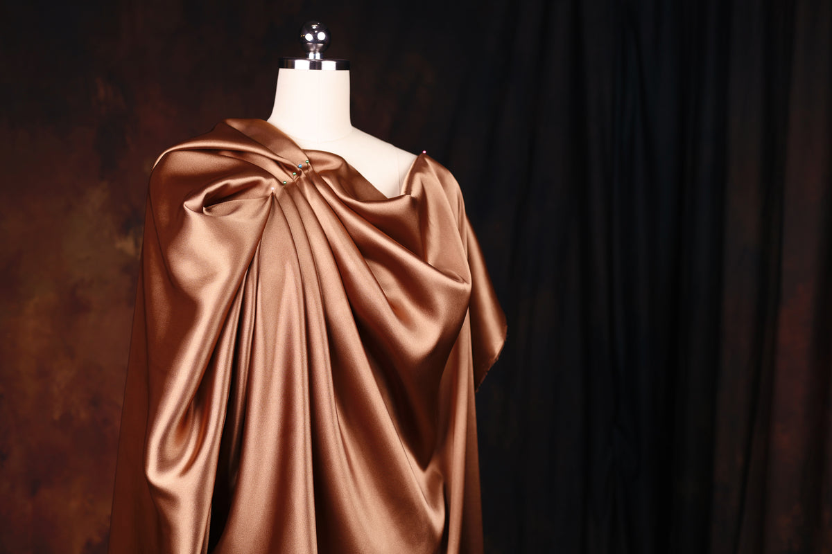 A mannequin wearing a gold-colored, draped dress stands against a dark background.