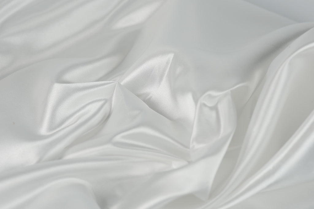 The image is a close-up of a white, flowing fabric, possibly silk or satin, with a soft, shiny texture.