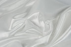 The image is a close-up of a white, flowing fabric, possibly silk or satin, with a soft, shiny texture.