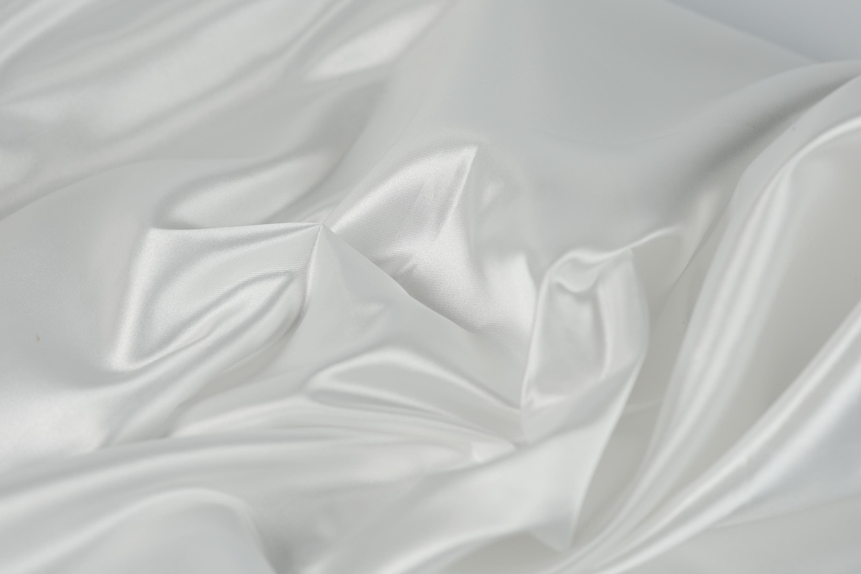 The image is a close-up of a white, flowing fabric, possibly silk or satin, with a soft, shiny texture.