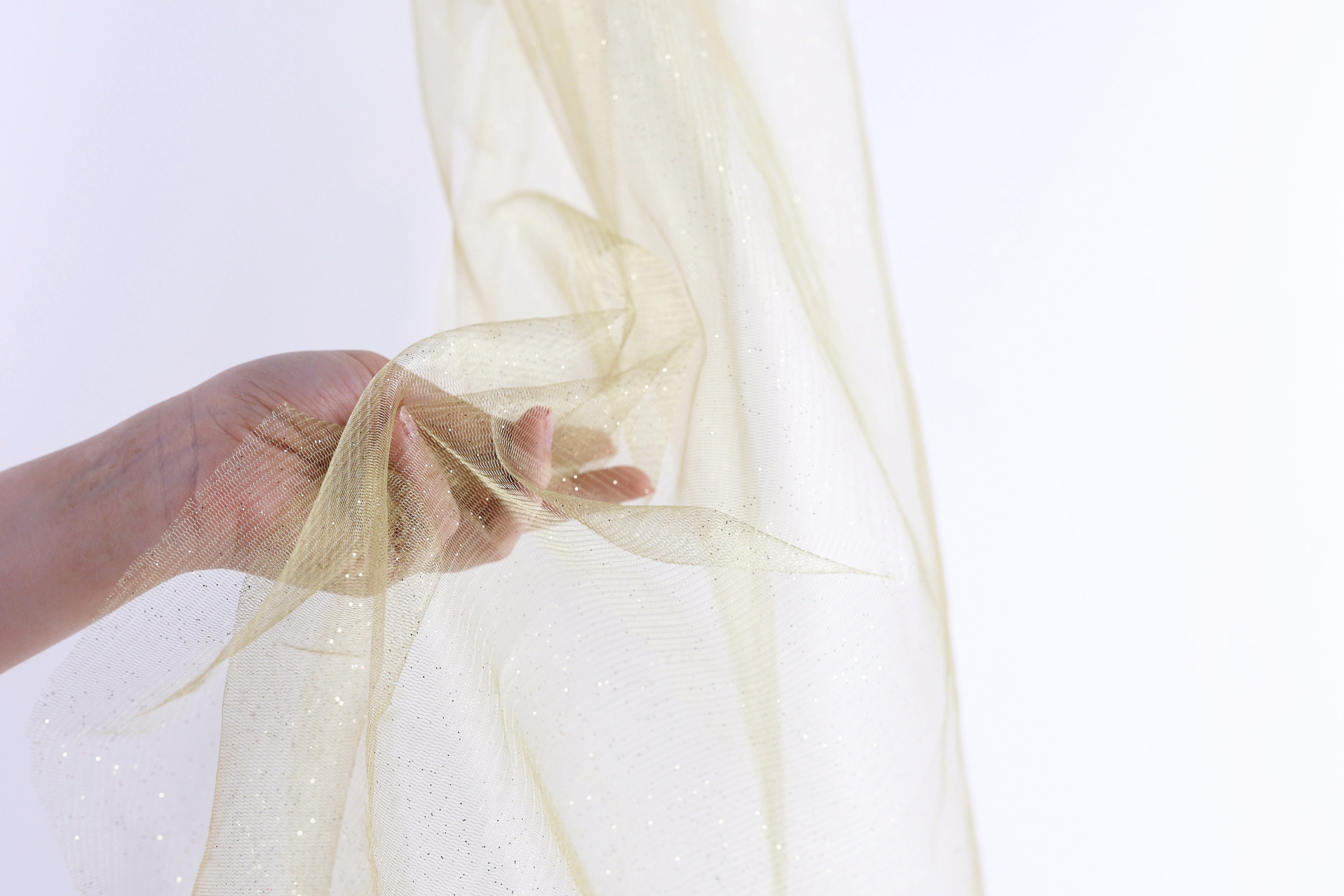 A hand is holding a piece of gold glittery fabric against a white background.