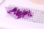 a clear ruler with a purple floral design placed on it, indicating a craft or sewing project.