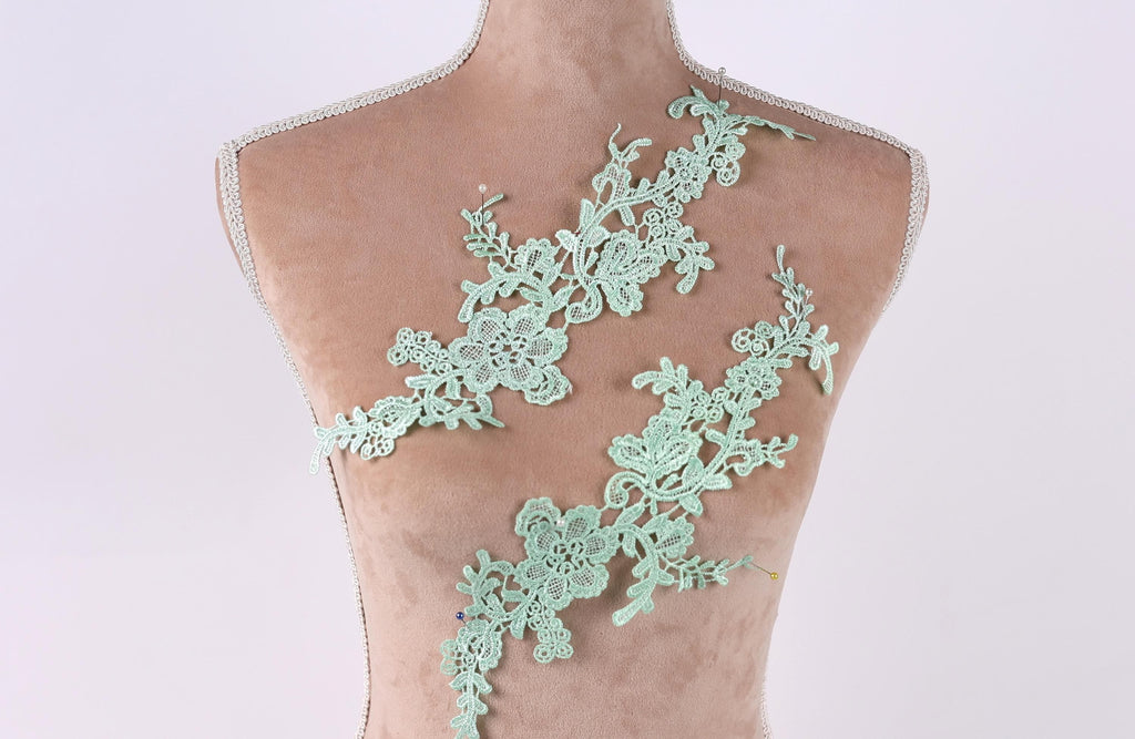 A mannequin torso with a green lace overlay, featuring intricate floral and leaf designs.