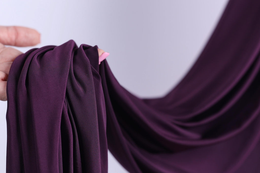 A hand is holding a piece of purple fabric, which appears to be a type of chiffon or sheer material.