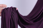 A hand is holding a piece of purple fabric, which appears to be a type of chiffon or sheer material.