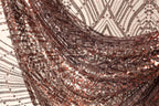 a close-up view of a fabric with a metallic, sequined texture. The fabric appears to be a dark brown color, with a pattern of small, shiny sequins covering it. The fabric is crumpled and wrinkled, giving it a textured, three-dimensional appearance.