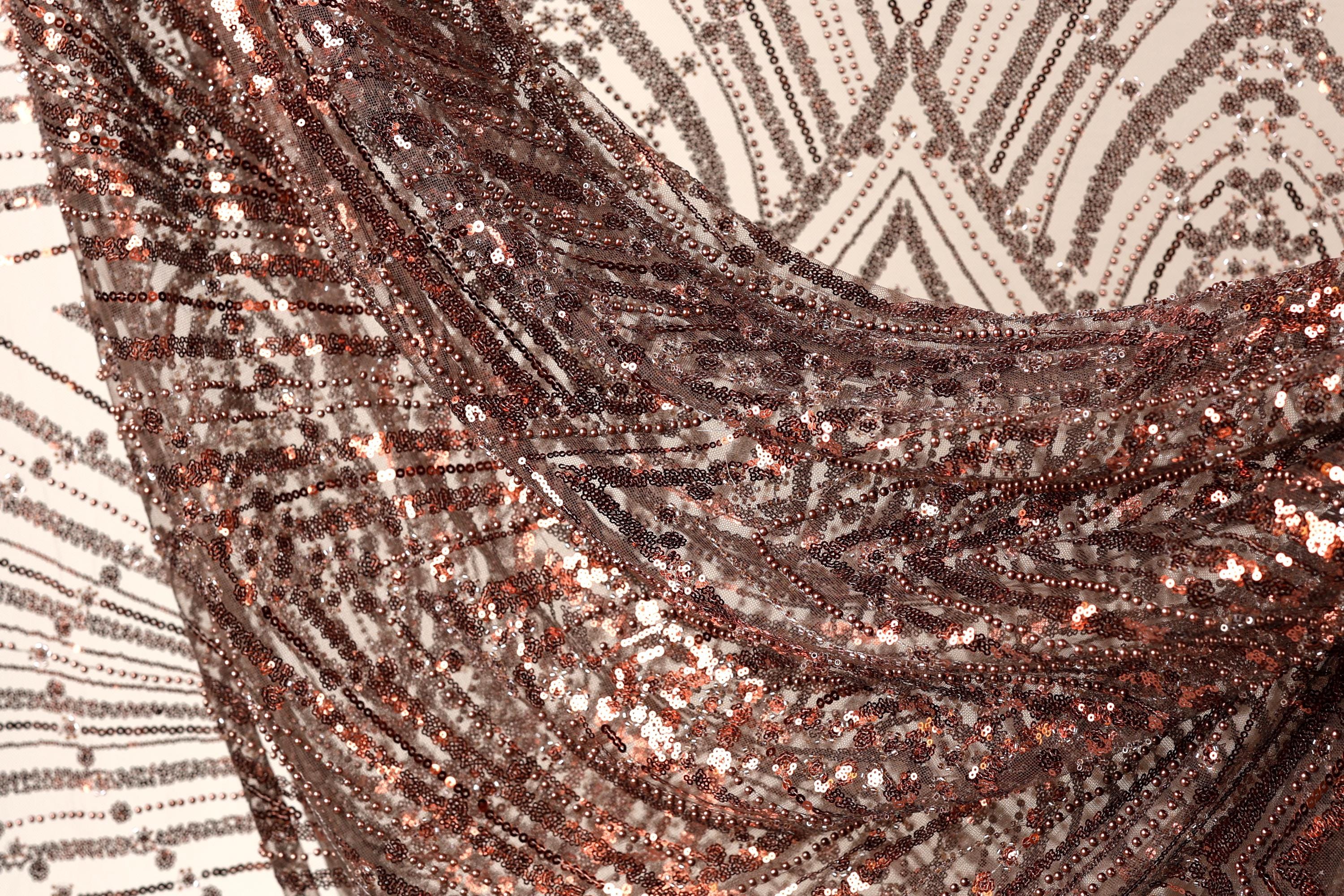 a close-up view of a fabric with a metallic, sequined texture. The fabric appears to be a dark brown color, with a pattern of small, shiny sequins covering it. The fabric is crumpled and wrinkled, giving it a textured, three-dimensional appearance.