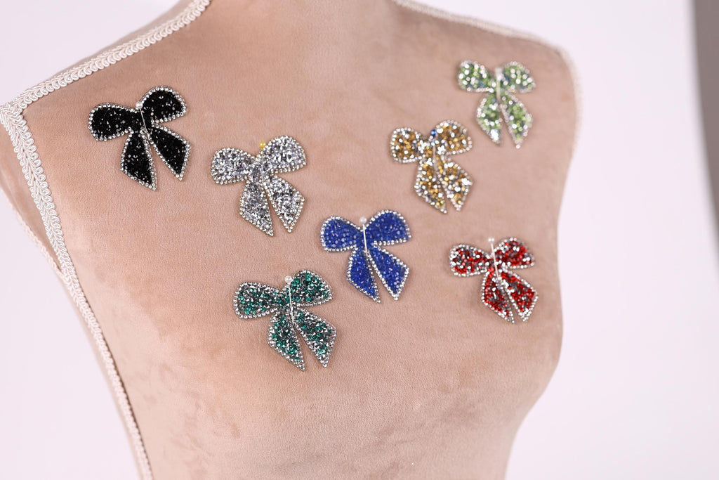 A mannequin bust with various colorful, sparkling rhinestone or crystal-like embellishments attached to it, including multiple bows and butterflies.