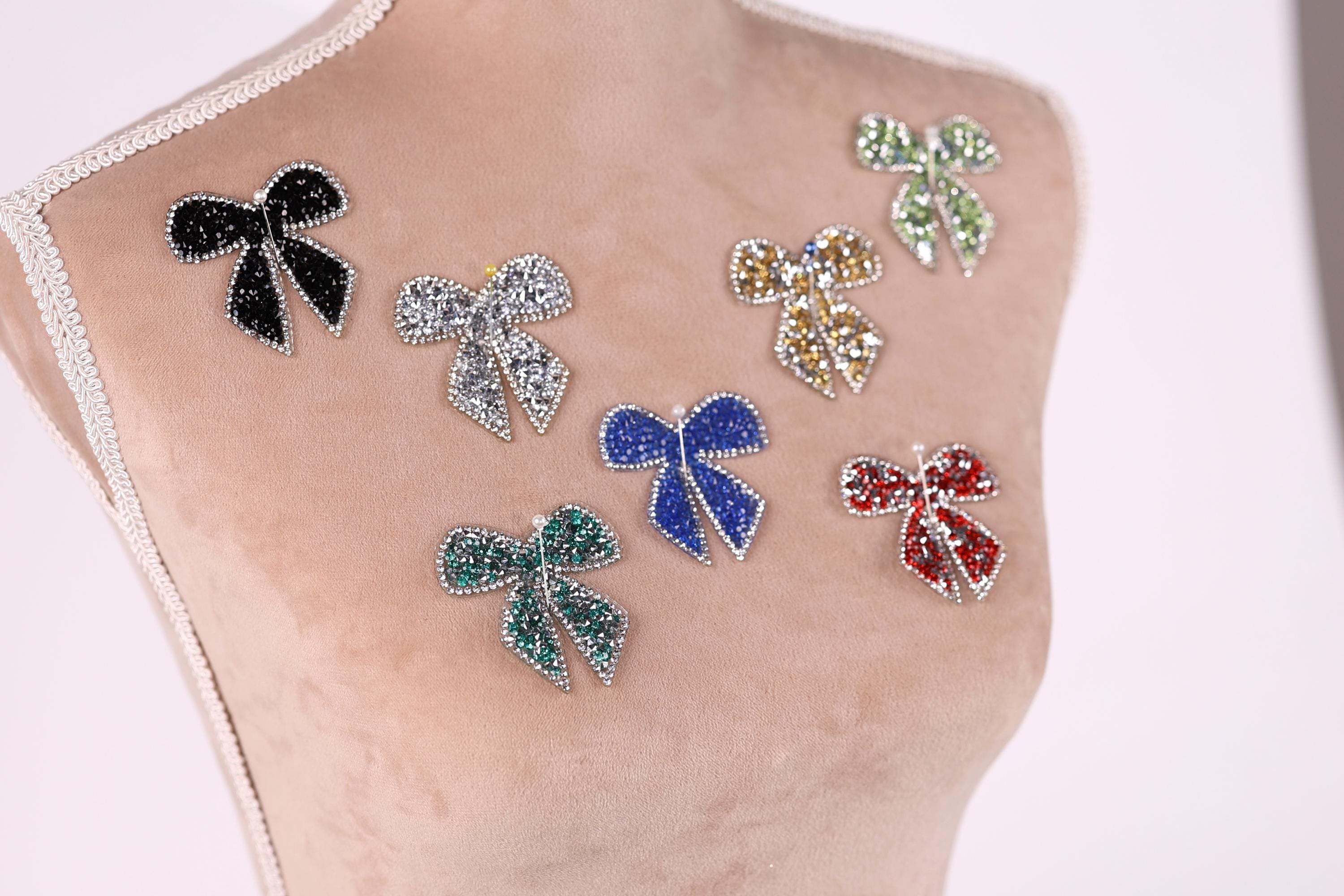 A mannequin bust with various colorful, sparkling rhinestone or crystal-like embellishments attached to it, including multiple bows and butterflies.