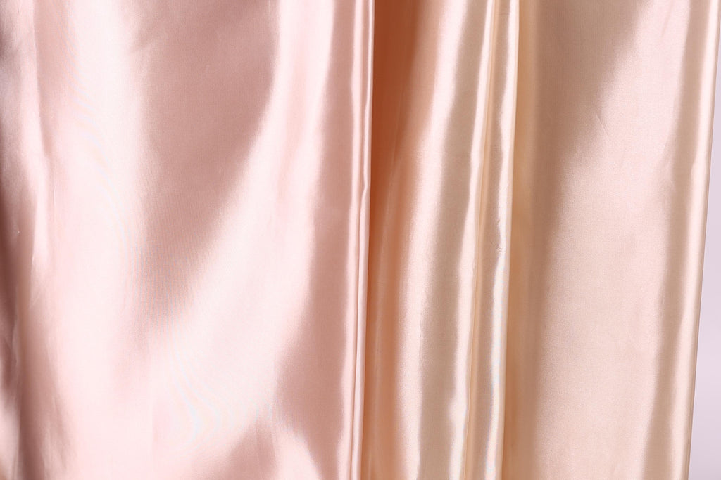 a close-up view of a soft, shiny fabric with a subtle gradient of colors, transitioning from a light pink to a darker peach. The fabric appears to be made of satin or a similar smooth, shiny material.