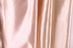 a close-up view of a soft, shiny fabric with a subtle gradient of colors, transitioning from a light pink to a darker peach. The fabric appears to be made of satin or a similar smooth, shiny material.