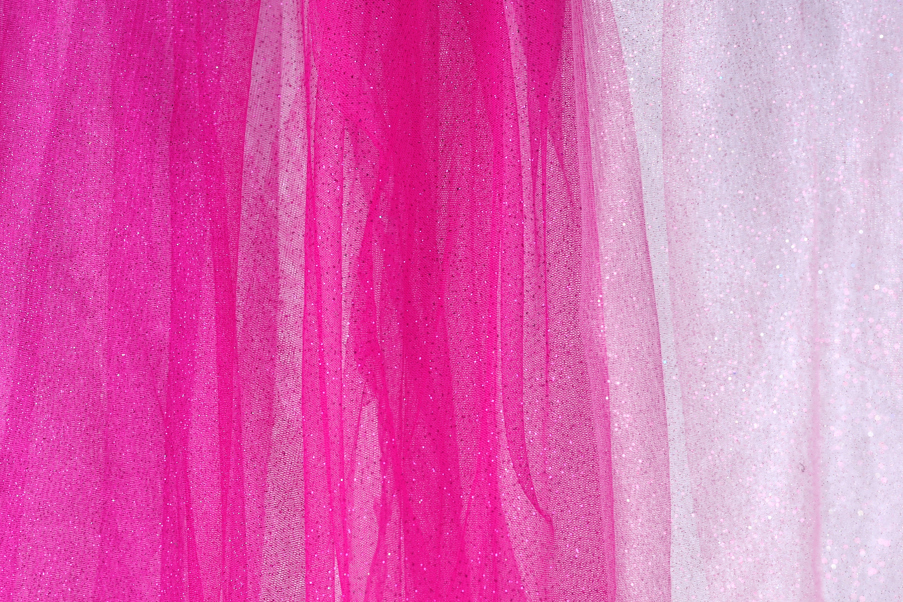 The image is a close-up of a fabric with a pink and white color scheme. The fabric appears to be a sheer material, with a pink hue dominating the background and a white hue in the foreground. The fabric has a textured appearance, with vertical lines and a slightly wrinkled texture.