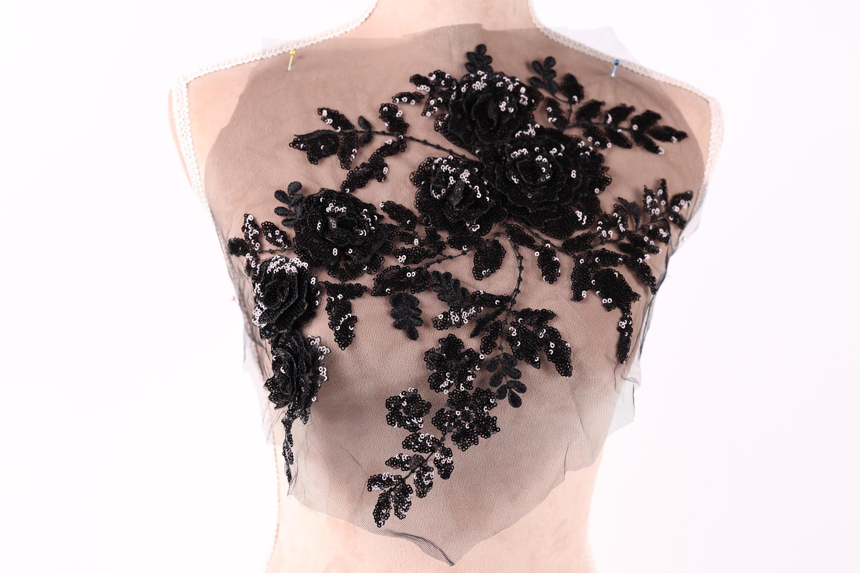 A mannequin torso with a sheer, black lace fabric covering the upper body. The fabric has a floral pattern with black sequins and leaves attached to it.