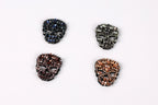 four ornate skull-shaped brooches, each with a unique color and design, arranged in a square formation against a white background.