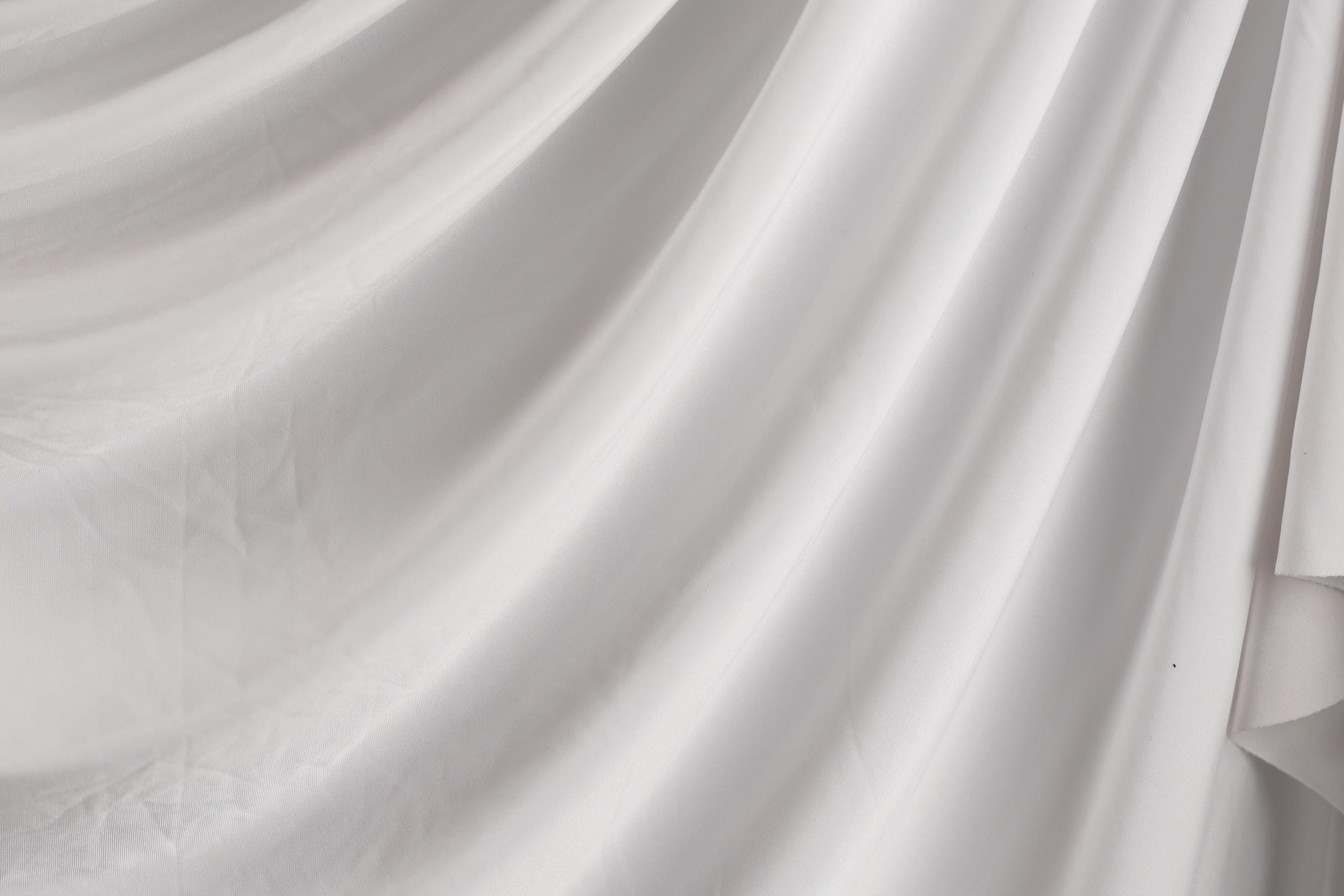 The image is a close-up of a white fabric, possibly a sheer or sheer-like material, with a soft, flowing texture.