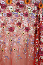 a vibrant and colorful floral embroidered fabric, with a variety of flowers in shades of pink, white, yellow, and orange. The fabric appears to be a sheer material, with the flowers hanging down in a cascading pattern. The overall design is visually striking and full of life, with the flowers creating a sense of movement and energy.