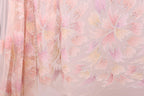 a close-up view of a delicate, pastel-colored fabric with a floral pattern. The fabric appears to be made of sheer material, giving it a soft and delicate appearance. The floral pattern consists of various shades of pink and yellow, creating a visually appealing and intricate design. The fabric is spread out, allowing for a clear and detailed view of its texture and pattern.