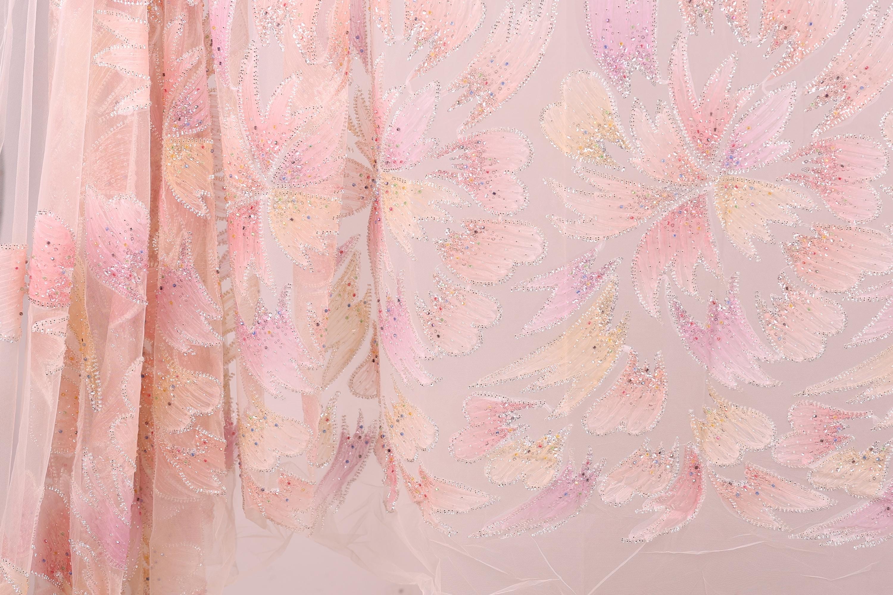 a close-up view of a delicate, pastel-colored fabric with a floral pattern. The fabric appears to be made of sheer material, giving it a soft and delicate appearance. The floral pattern consists of various shades of pink and yellow, creating a visually appealing and intricate design. The fabric is spread out, allowing for a clear and detailed view of its texture and pattern.
