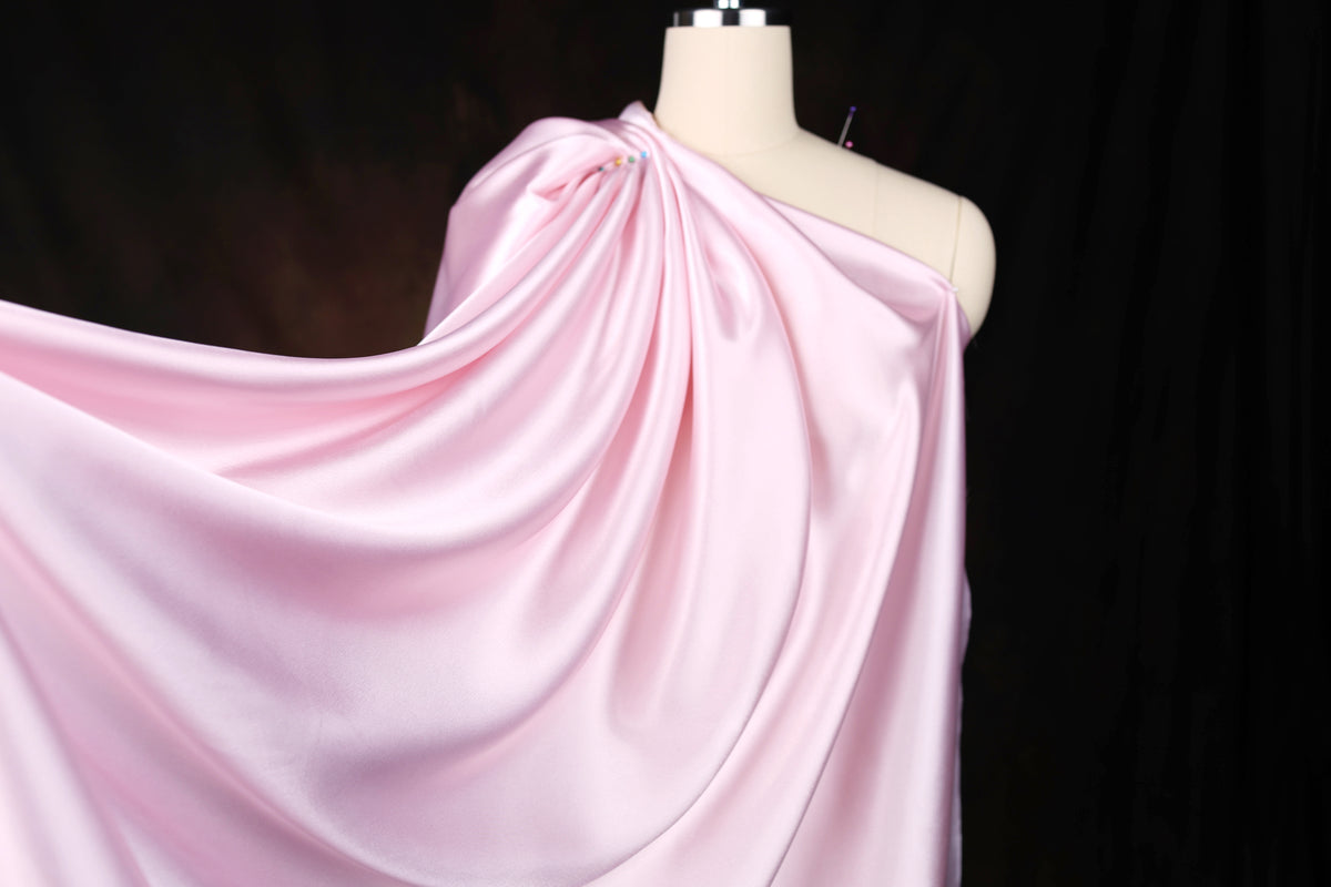 A mannequin wearing a flowing, pink satin dress against a dark background.