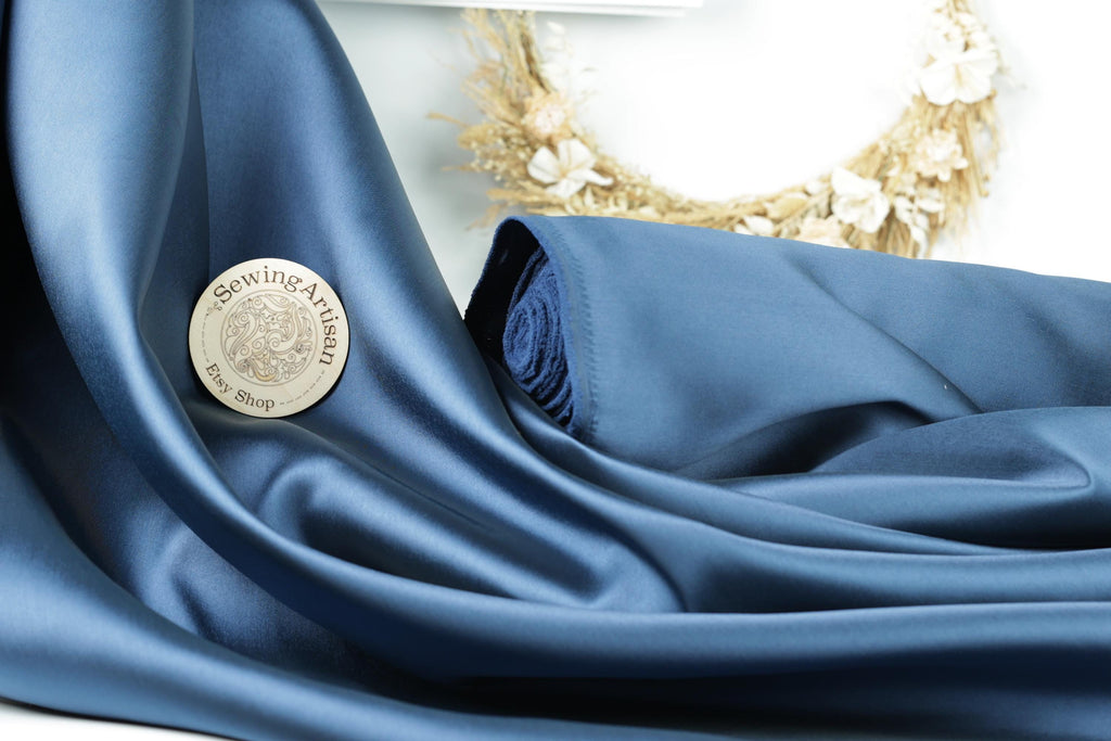 a blue satin fabric with a sewing artisan's pin resting on it.