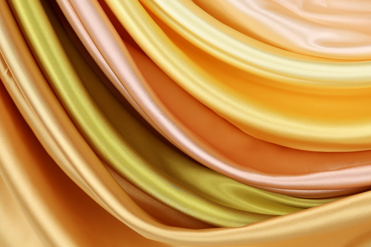 a close-up view of a variety of colorful satin fabric, including shades of yellow, orange, and green.
