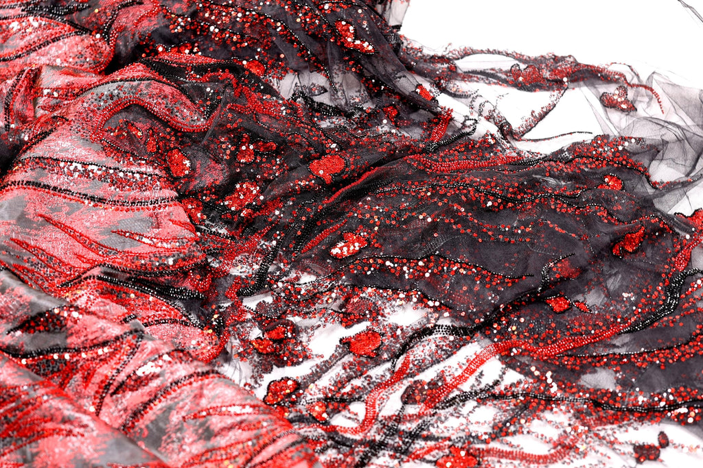 The image is a close-up of a fabric with a striking pattern of red and black sequins and lace. The fabric appears to be a sheer material, with a mix of black and red colors. The pattern is intricate and detailed, with the sequins and lace adding texture and depth to the fabric. The image does not contain any discernible objects or actions, and the focus is solely on the fabric and its design.