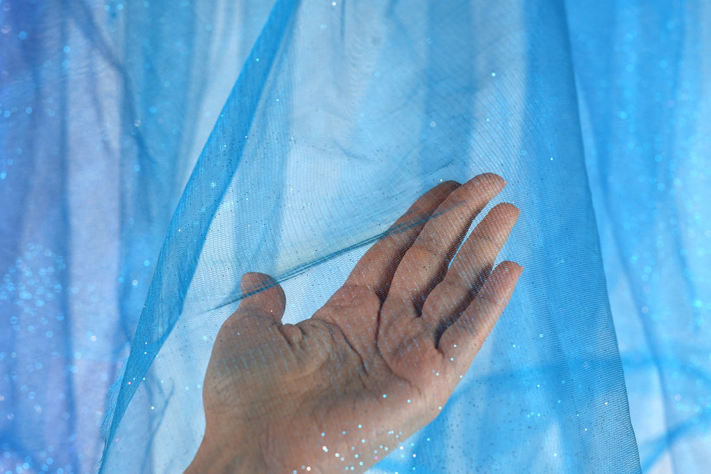 A hand is holding up a blue mesh fabric against a blue background.