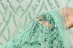 A hand is holding a piece of fabric with a green sequin pattern, which appears to be a decorative textile.