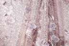 The image is a close-up of a delicate, shimmering fabric with a floral pattern. The fabric appears to be made of sequins and lace, creating a visually striking and intricate design.